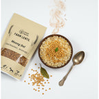 Mye Farm Desi Roasted Moong Dal product packaging next to a wooden bowl of khichdi or rice and dal. The image features a vintage spoon, scattered roasted moong dal grains, a bay leaf, and an aroma graphic, suggesting a wholesome and aromatic meal.